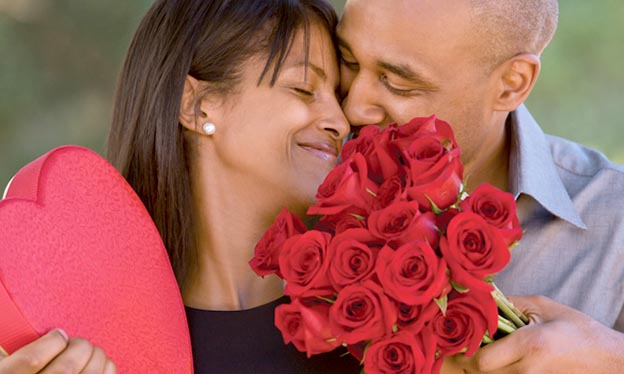 Man and woman embracing with red roses and heart shaped box of candy